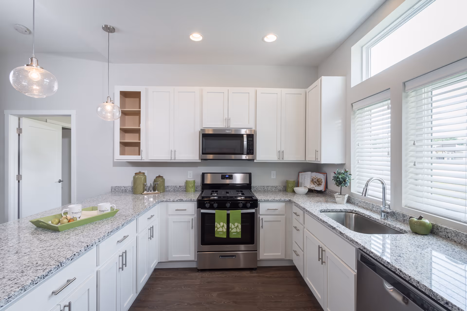 Bright modern kitchen with white cabinets, granite countertops, stainless steel stove and microwave, and a sink under a window.