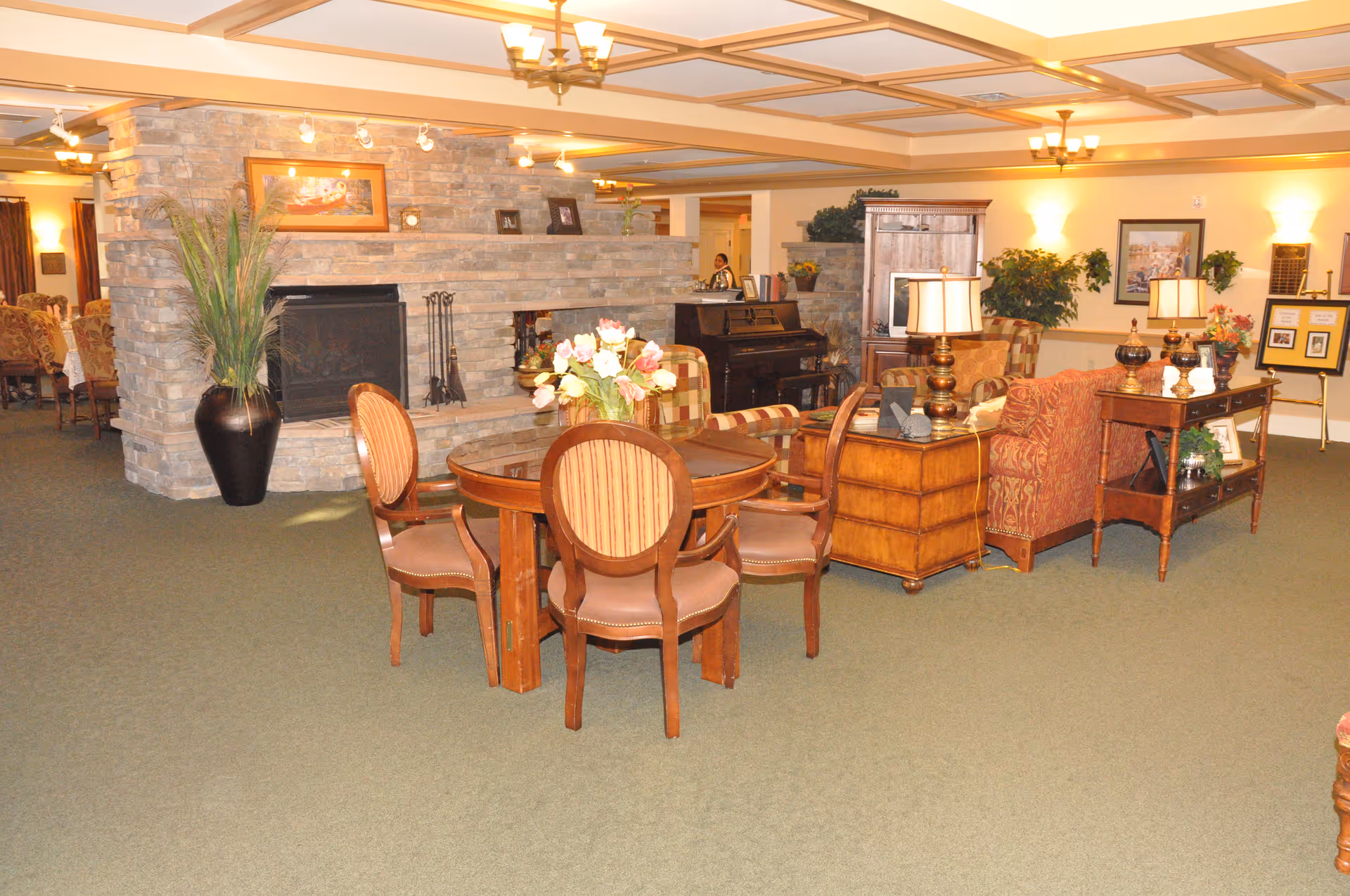 Cozy communal living area with a round table and chairs, sofas, lamps, and a stone fireplace.
