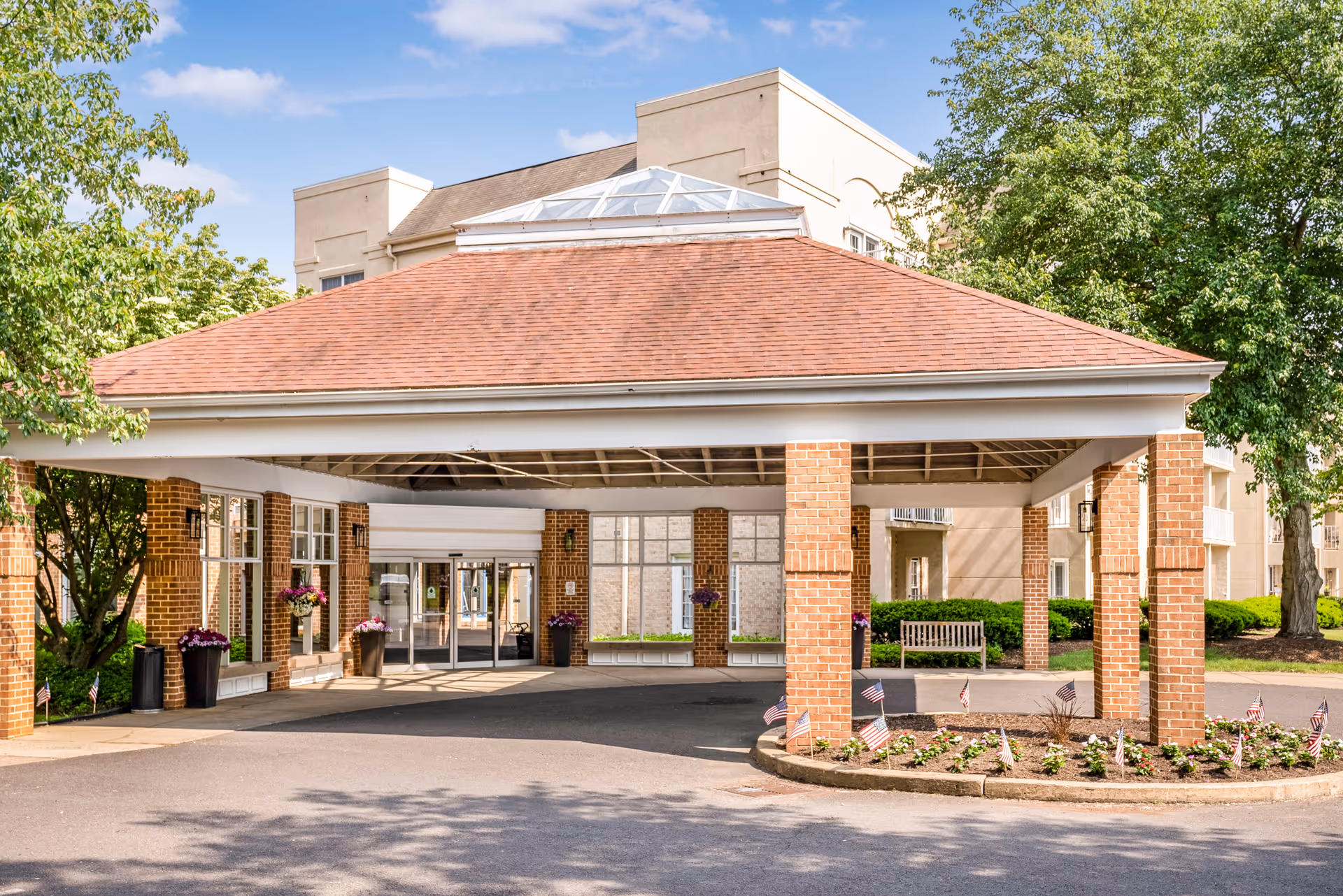 Covered porte-cochère with brick columns and a driveway leading to the front entrance of a multi-story senior living building.