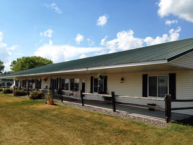Single-story senior living facility exterior with green roof, porch, and railing along walkway.