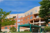 Front exterior of a multi-story retirement community building with balconies, a covered entrance, and an American flag.