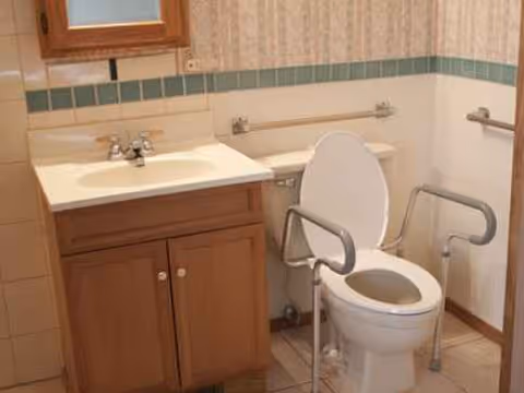 Bathroom with sink, cabinet, mirror, and safety grab bars beside the toilet.