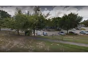 View of a parking lot with several cars parked, surrounded by trees and greenery under a partly cloudy sky.