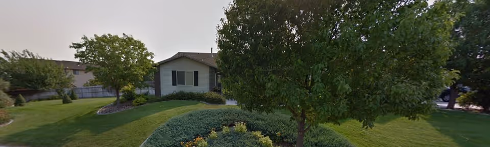 Single-story building partially hidden by trees with a manicured lawn and shrub beds in front.