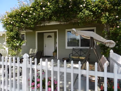 Front porch of a single-story senior living facility with a swing and flowering vines.