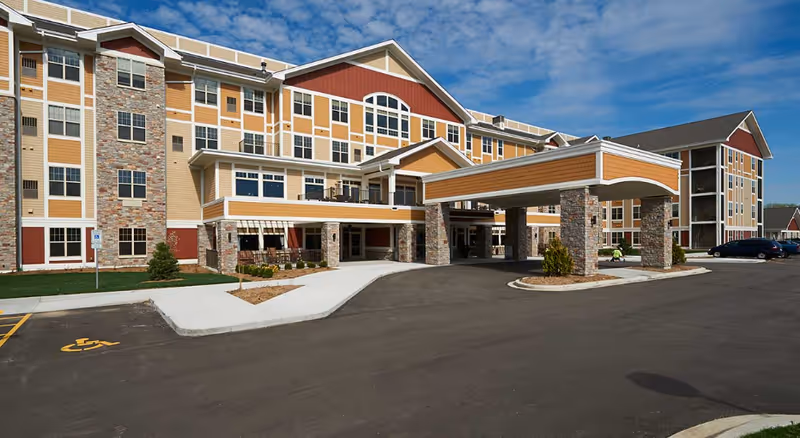 Front exterior of a multi-story senior living building with a covered drop-off canopy and paved driveway.