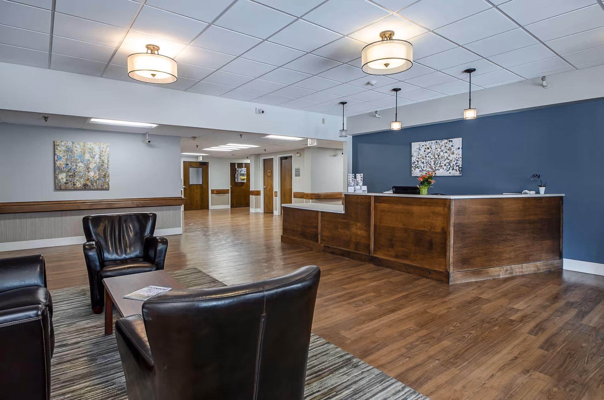 Spacious reception lobby with a wooden check-in desk, leather chairs around a coffee table, and pendant lighting.