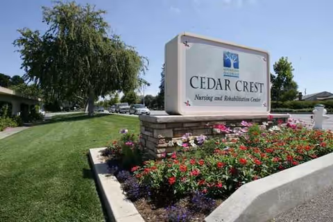 Cedar Crest Nursing and Rehabilitation Center entrance sign with colorful flower bed and green lawn.