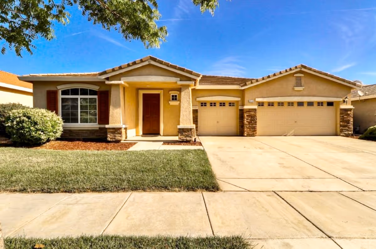 Single-story suburban house with a three-car garage, front lawn and driveway under a blue sky.