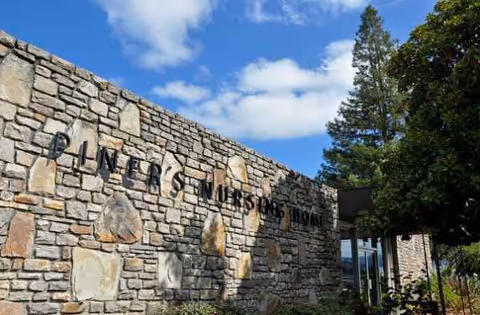 Stone exterior wall with signage reading Piners Guest Home and trees against a blue sky.