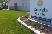 A lawn and flower bed in front of a sign reading "Georgia Manor Nursing & Rehabilitation" with the building exterior visible behind it.