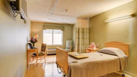 Single-bed patient room at South Holland Manor Health & Rehab with desk, chairs, and window.
