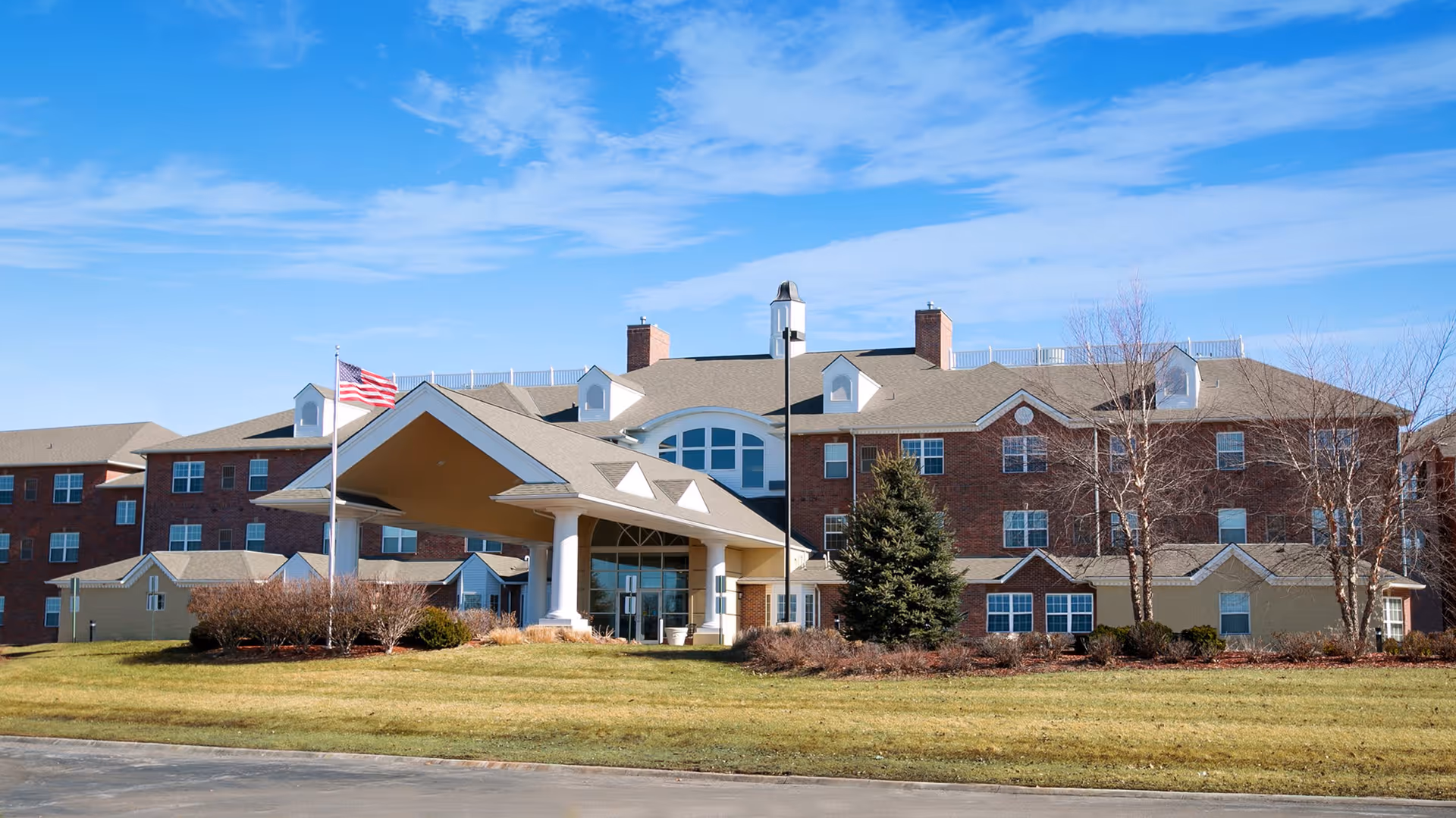 Front exterior view of Walnut Grove Retirement Community building with a large covered entrance, American flag on a flagpole, and a well-maintained lawn under a blue sky.