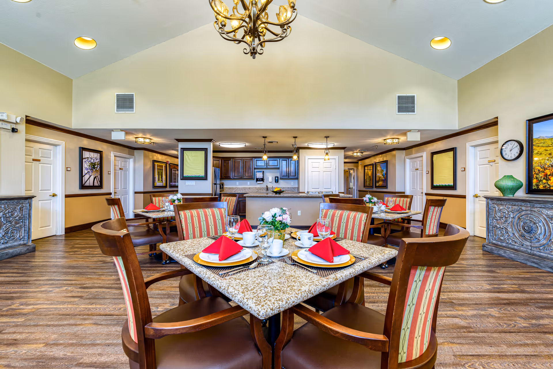 Bright communal dining room with set tables, striped chairs, granite tabletops, and an open kitchen in the background.