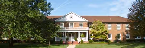Brick two-story senior living facility with a white porch and green lawn.