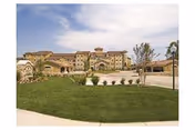 Front view of a Mediterranean-style residential building with a circular driveway, landscaped lawn, and blue sky.