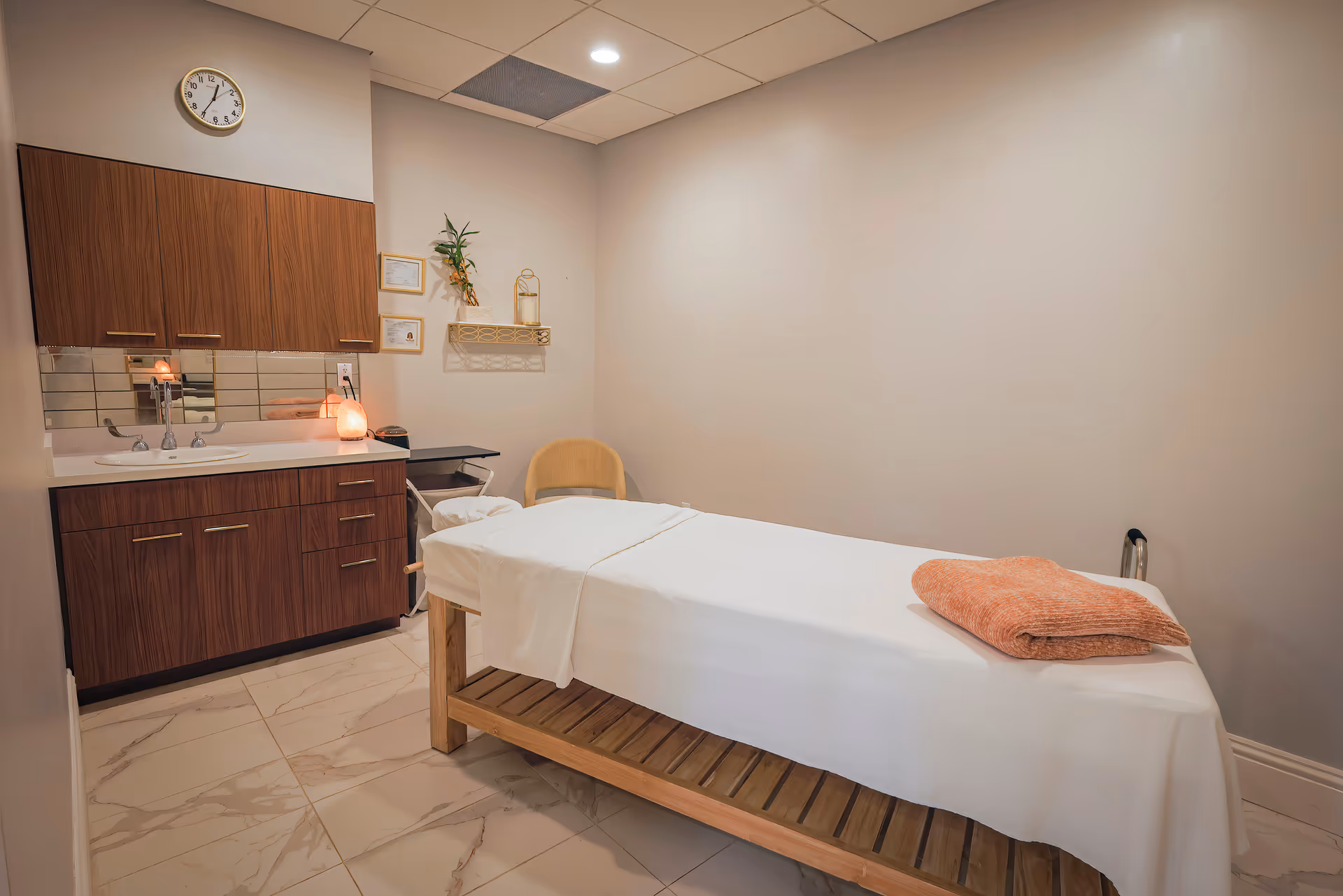 A calm spa/treatment room with a massage table draped in white linens, wooden cabinets and a sink against the wall.