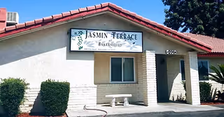 Front exterior of Jasmin Terrace at El Molino, a single-story building with a sign, window, and a bench outside.