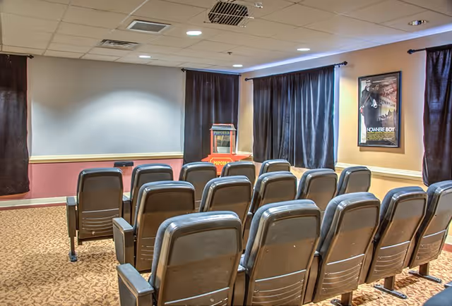 Small screening room with rows of theater seats facing a blank projection screen and a popcorn machine.