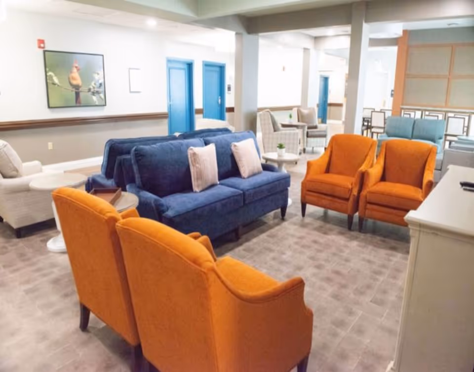 Communal lounge with a blue sofa, several orange armchairs, side tables, and wall artwork.