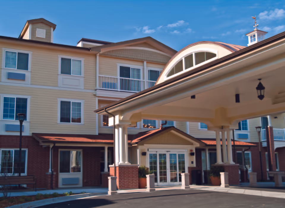 Front entrance of a multi-story senior living building with a covered porte-cochère and brick-and-siding facade.