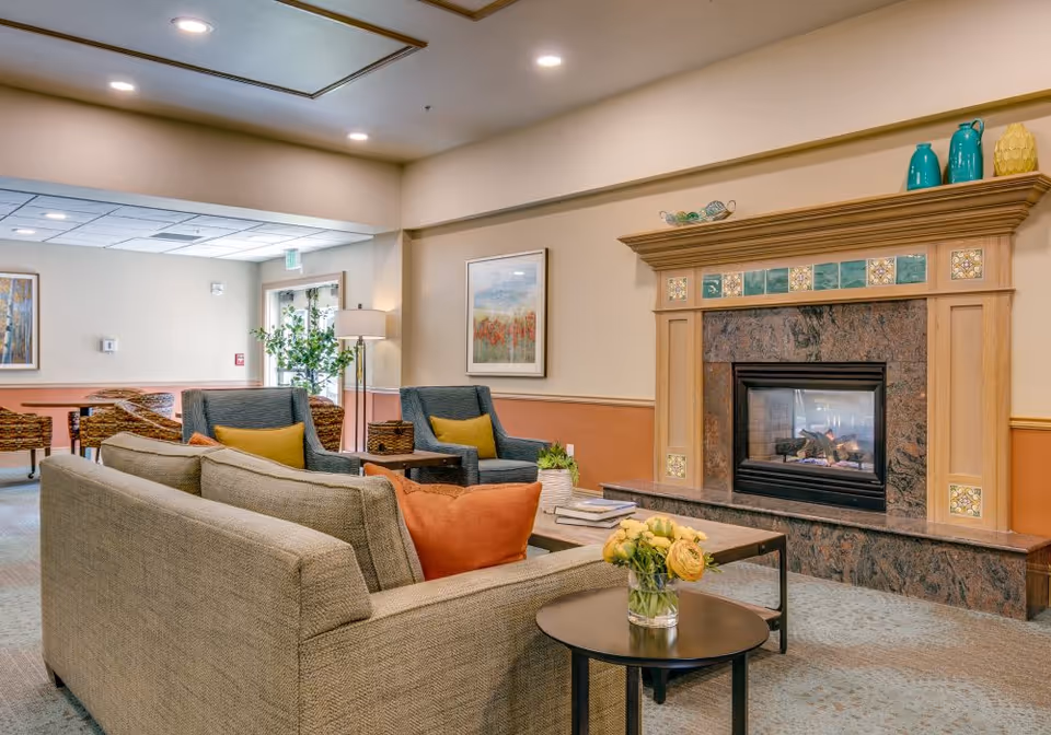 A cozy common lounge with sofas and armchairs arranged around a coffee table in front of a decorative fireplace.
