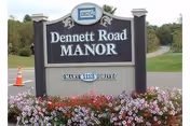 Outdoor sign for Dennett Road Manor with a colorful flower bed in front.