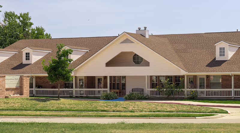 Front exterior of a single-story senior living building with a covered porch, bench, and pitched roof.