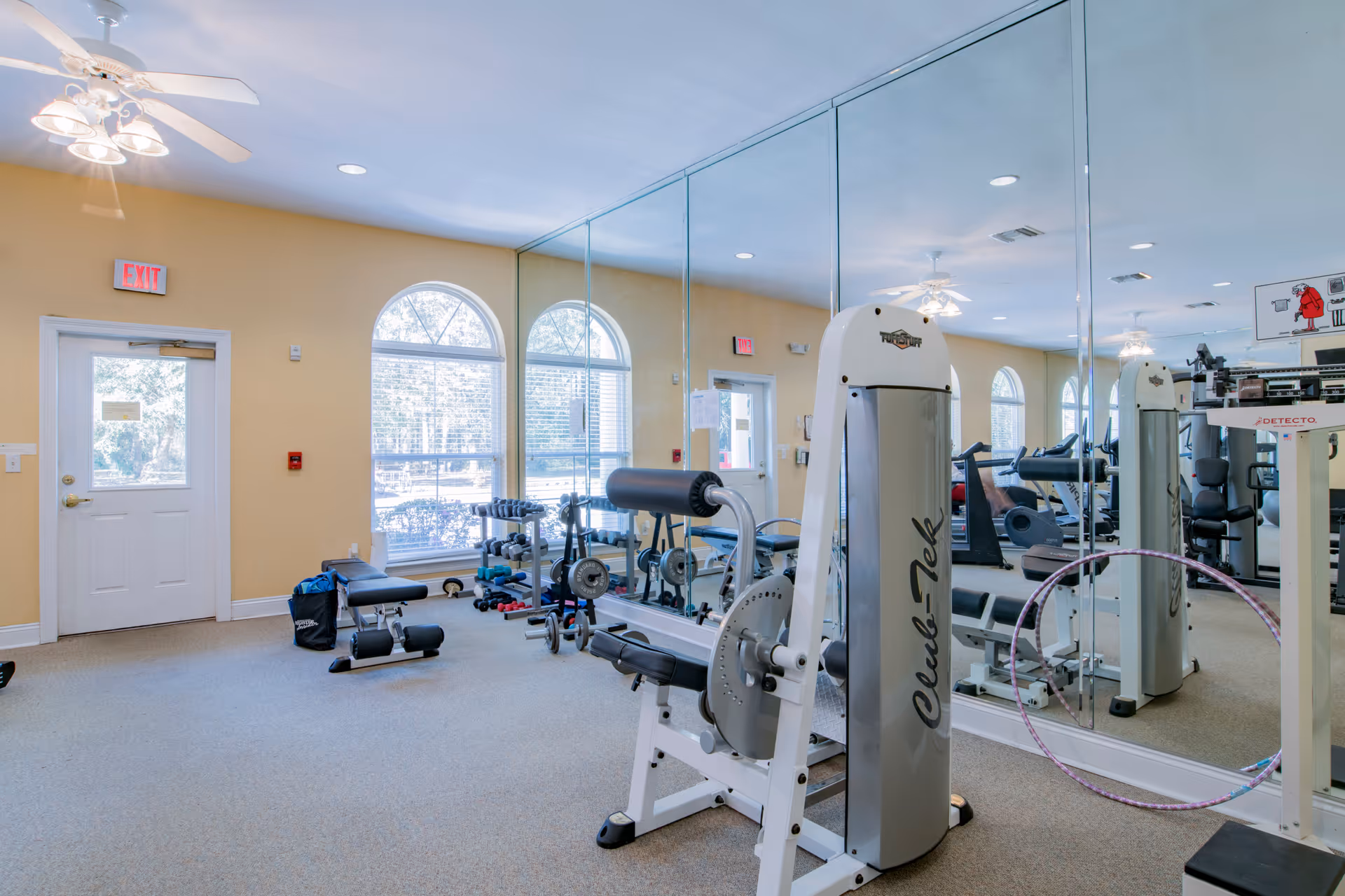 Exercise room with weight machines, free weights, a mirrored wall and arched windows.