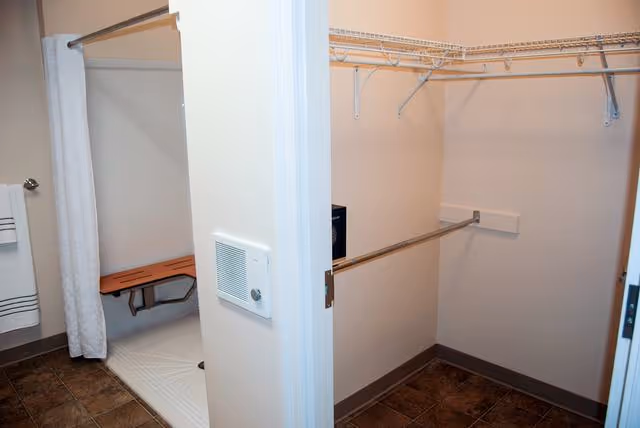 A bathroom showing a walk-in shower with a bench and curtain next to an empty walk-in closet with wire shelving and hanging rods.