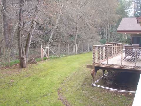 A wooden deck attached to a house with a grassy yard and trees.