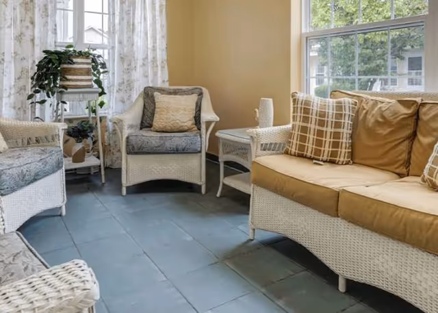 Bright sitting area with white wicker chairs and a cushioned sofa by windows and a small side table.