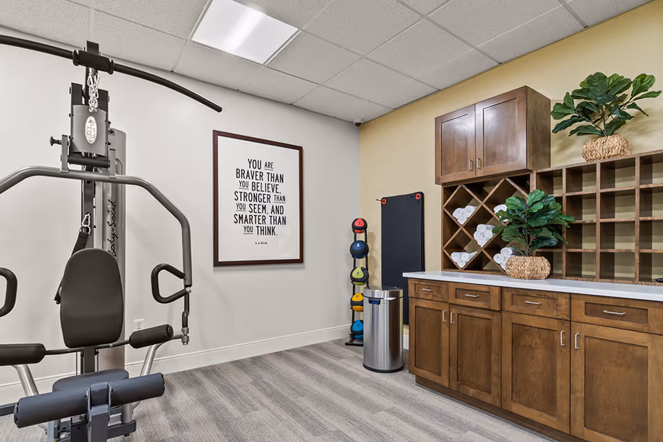Small fitness room with a multi-station exercise machine, stacked kettlebells, towel cubbies and wooden cabinetry.