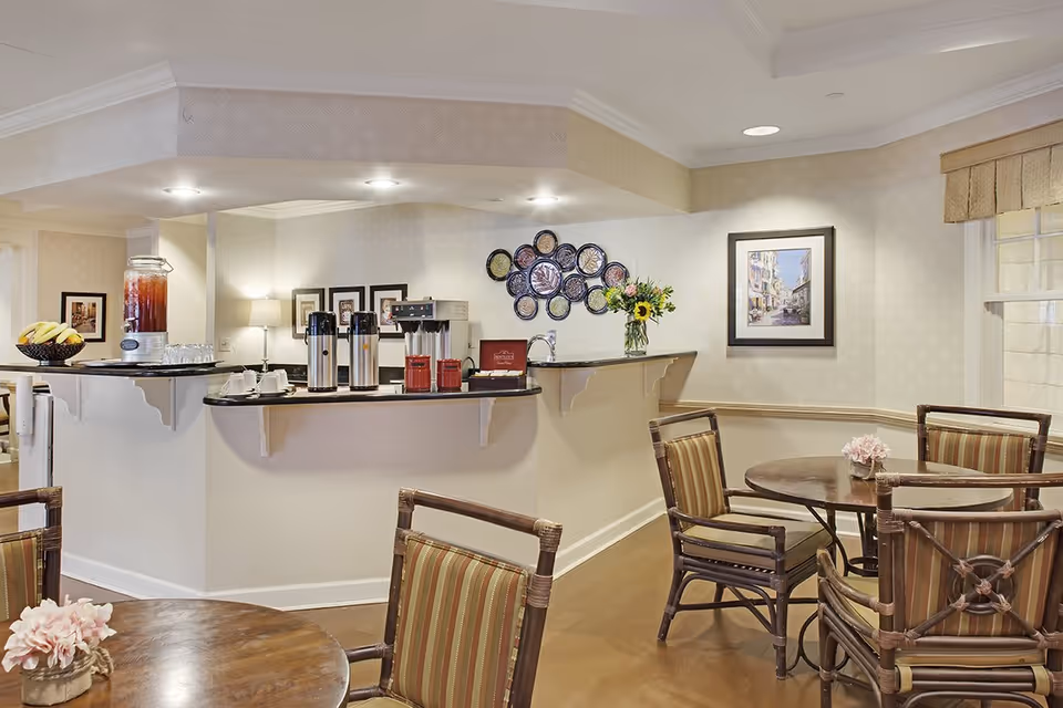 Bright communal dining area with round tables and chairs and a beverage counter offering coffee and juice.