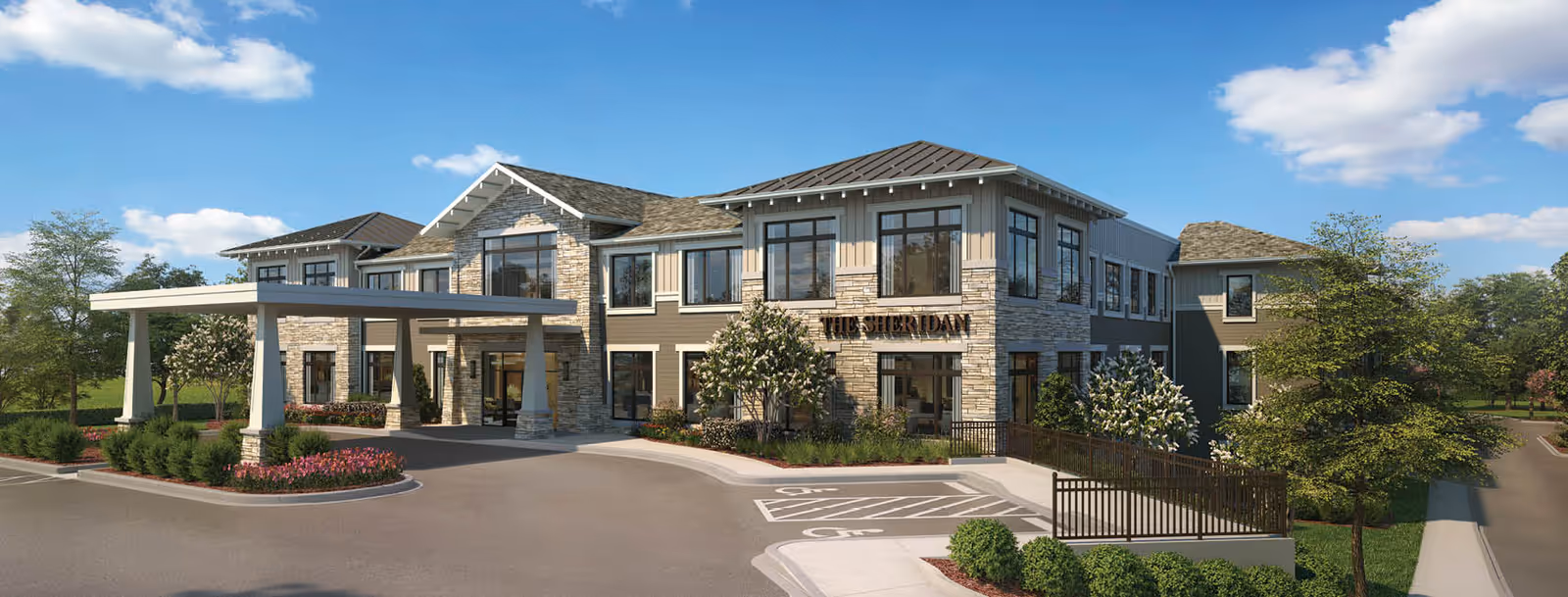 Two-story senior living building labeled "The Sheridan" with a covered entrance, landscaped driveway, and a blue sky.