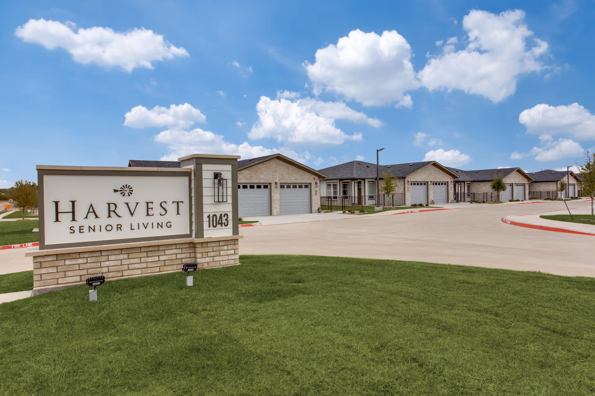 Exterior view of Harvest Senior Living: sign, driveway, and row of campus buildings.