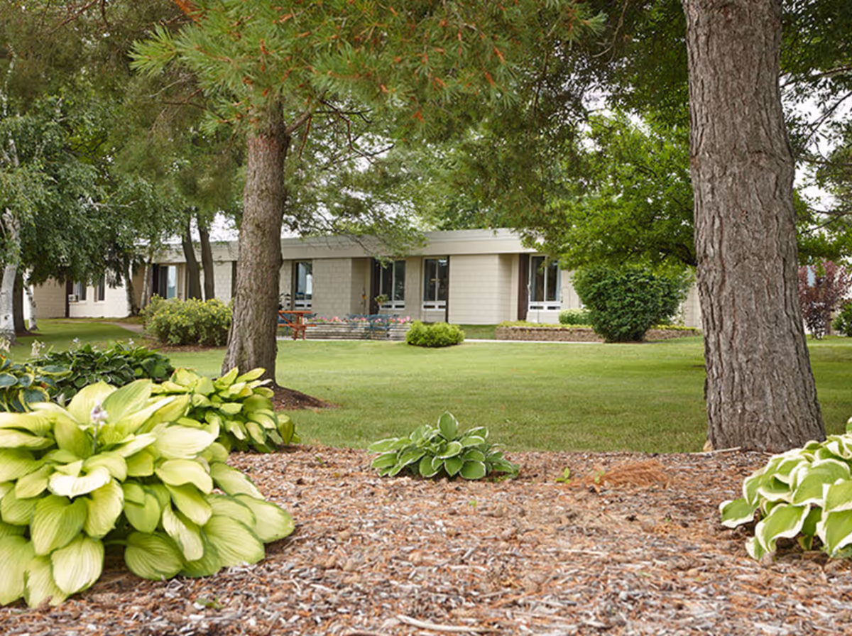 Landscaped lawn with trees and shrubs in front of a single-story facility building.
