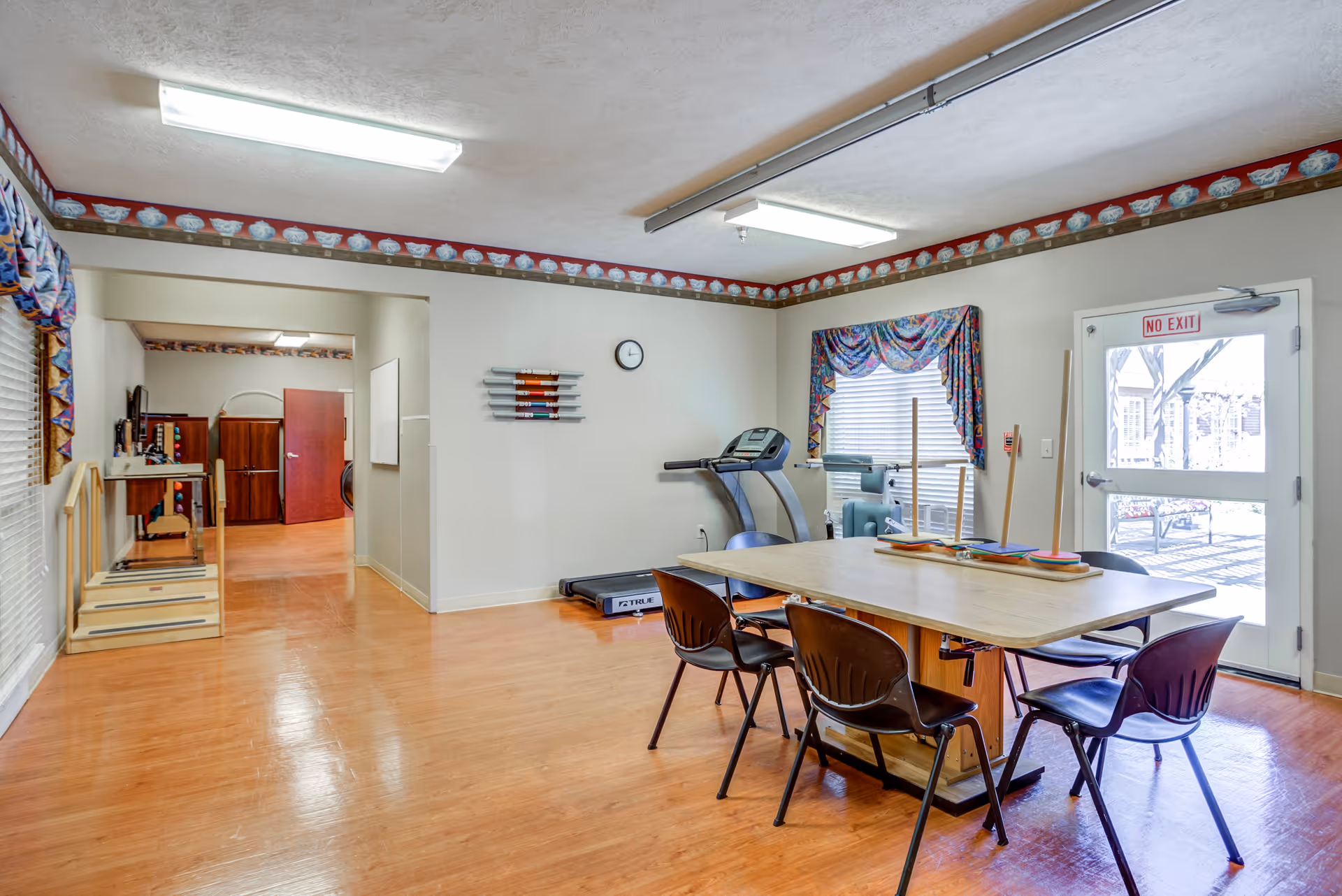 A bright multipurpose interior room with a table and chairs, exercise equipment, and a door to the outside.