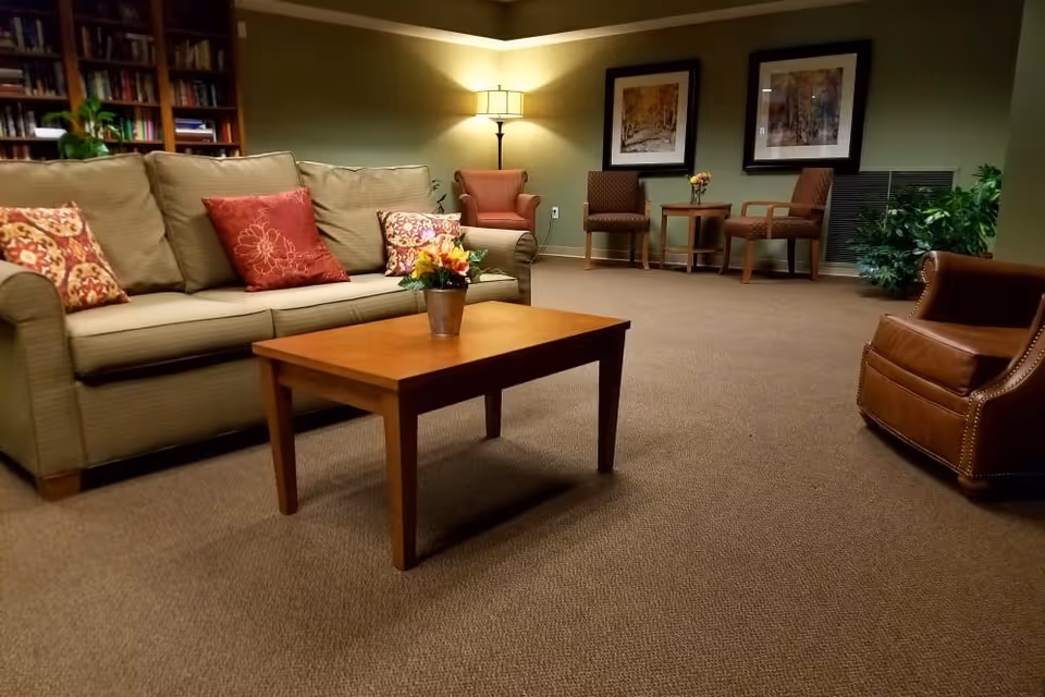 Cozy lounge area with a sofa, coffee table, armchairs, floor lamp, bookshelves and framed artwork on the walls.