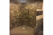 Open tiled walk-in shower with marble-patterned walls, multiple stainless grab bars, and a floor drain.