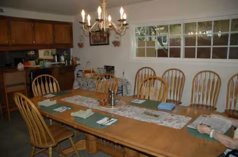 A long dining table with wooden chairs under a chandelier in a resident dining room.