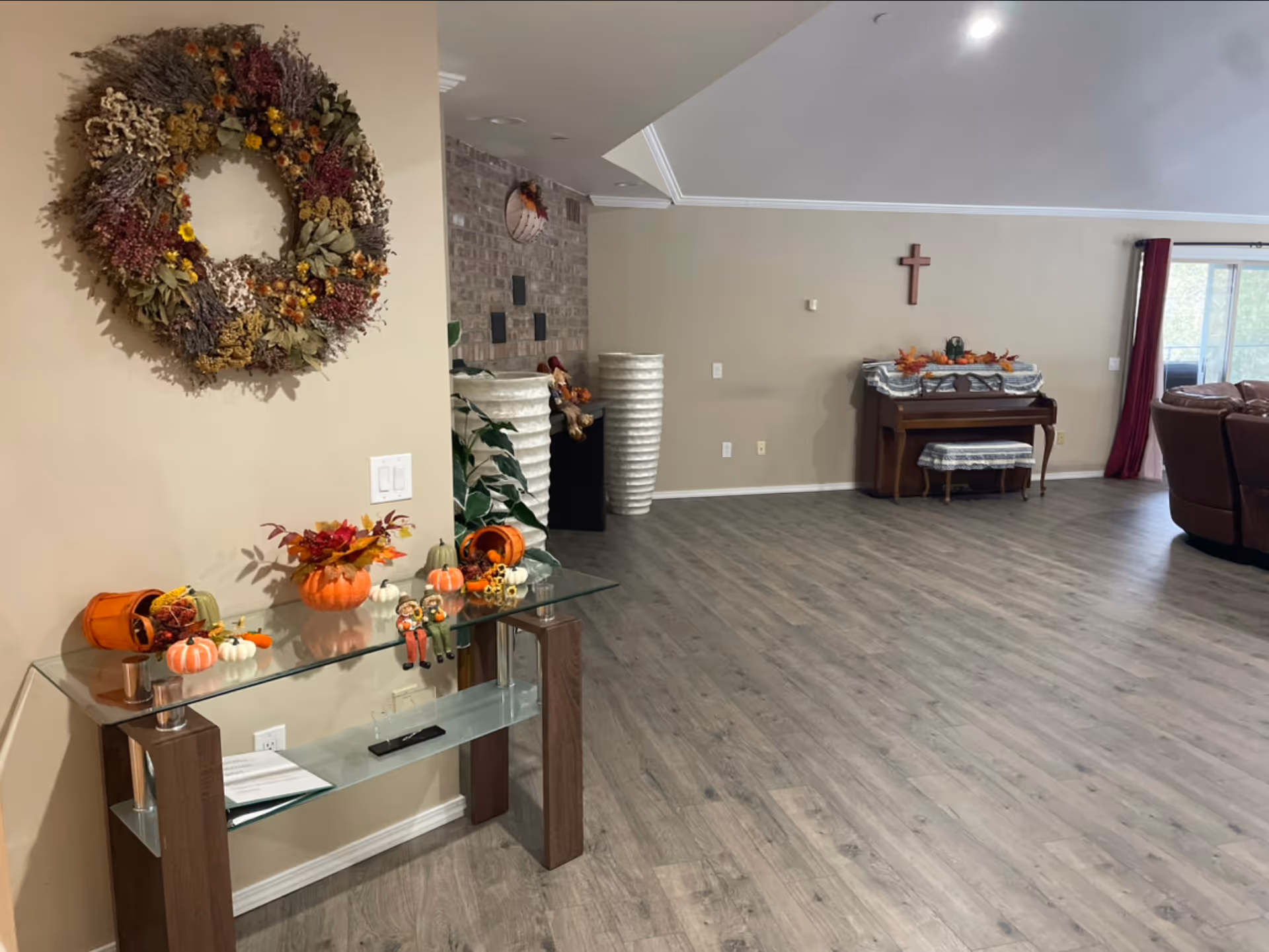 Spacious living room interior with wood floors, a wreath and glass console table decorated for fall, a piano against the far wall and seating to the right.