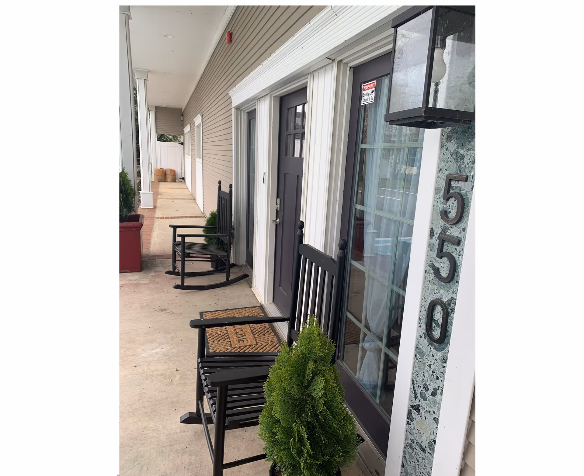 Exterior corridor of Loving Care Assisted Living IV with black rocking chairs along doors.