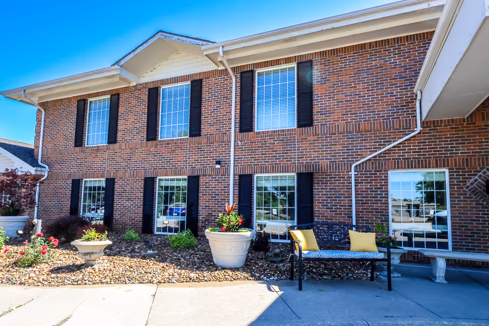 Brick senior living facility exterior with windows, planters, and a bench.