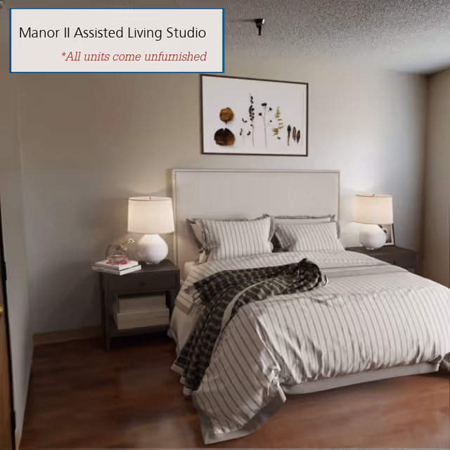 A neatly made bed with striped bedding and pillows in a studio apartment. There are two bedside tables, each with a white lamp. Above the bed is a framed artwork featuring dried plants. The room has wooden flooring and neutral-colored walls. A text box in the upper left corner reads 'Manor II Assisted Living Studio *All units come unfurnished'.