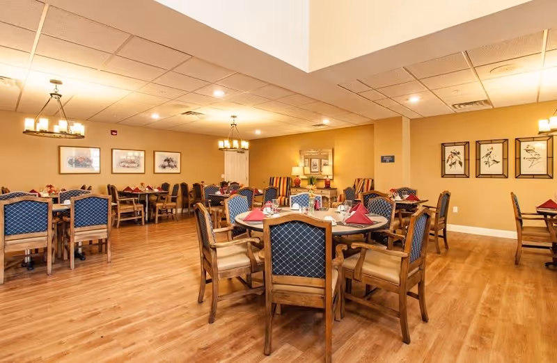 Spacious dining room with multiple round and rectangular tables set with napkins and wooden chairs on a wood floor.