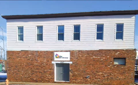 Two-story building with white siding above brick facade and a centered entrance.