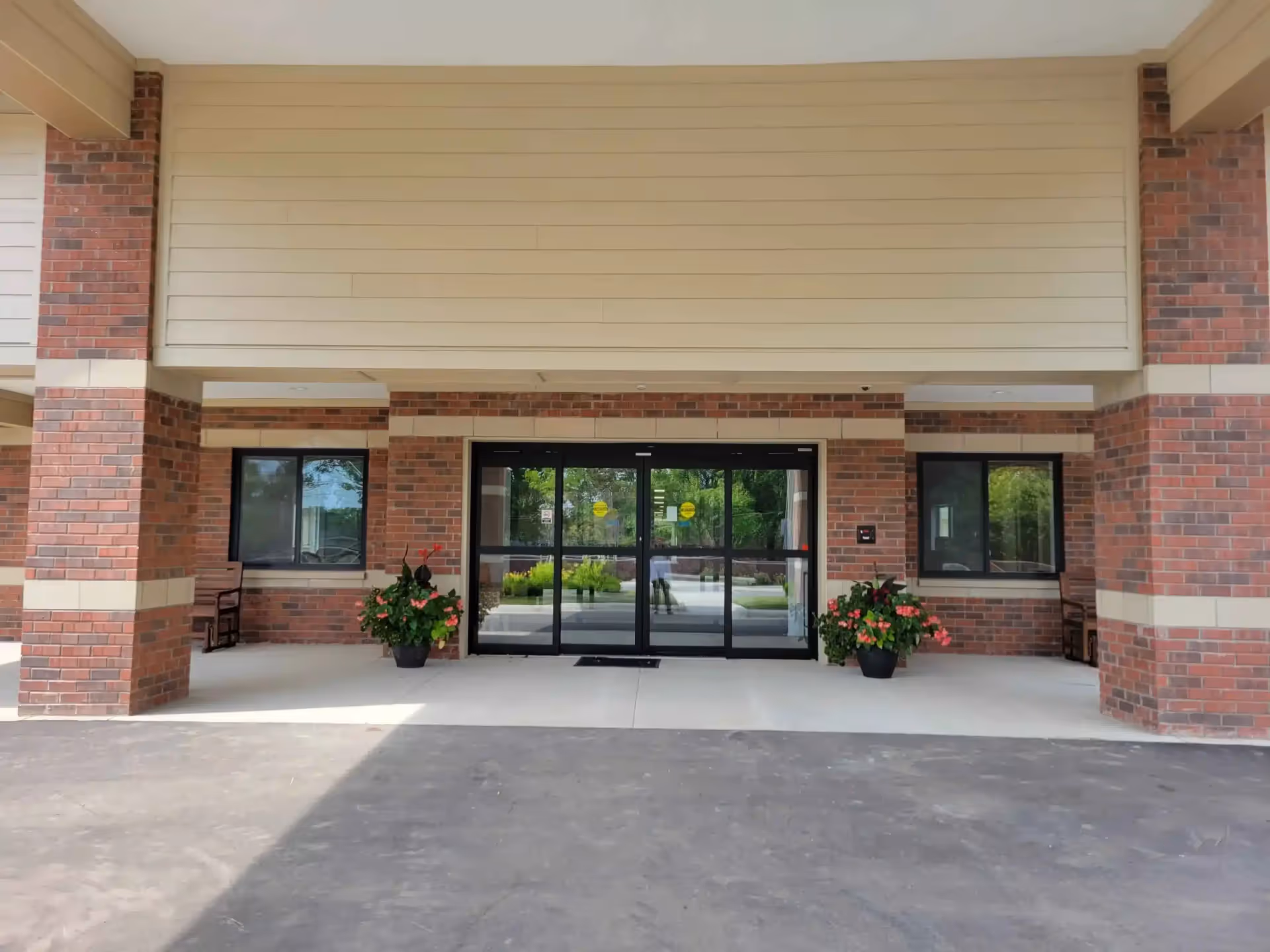 Brick exterior entrance with glass doors, columns, and potted plants.