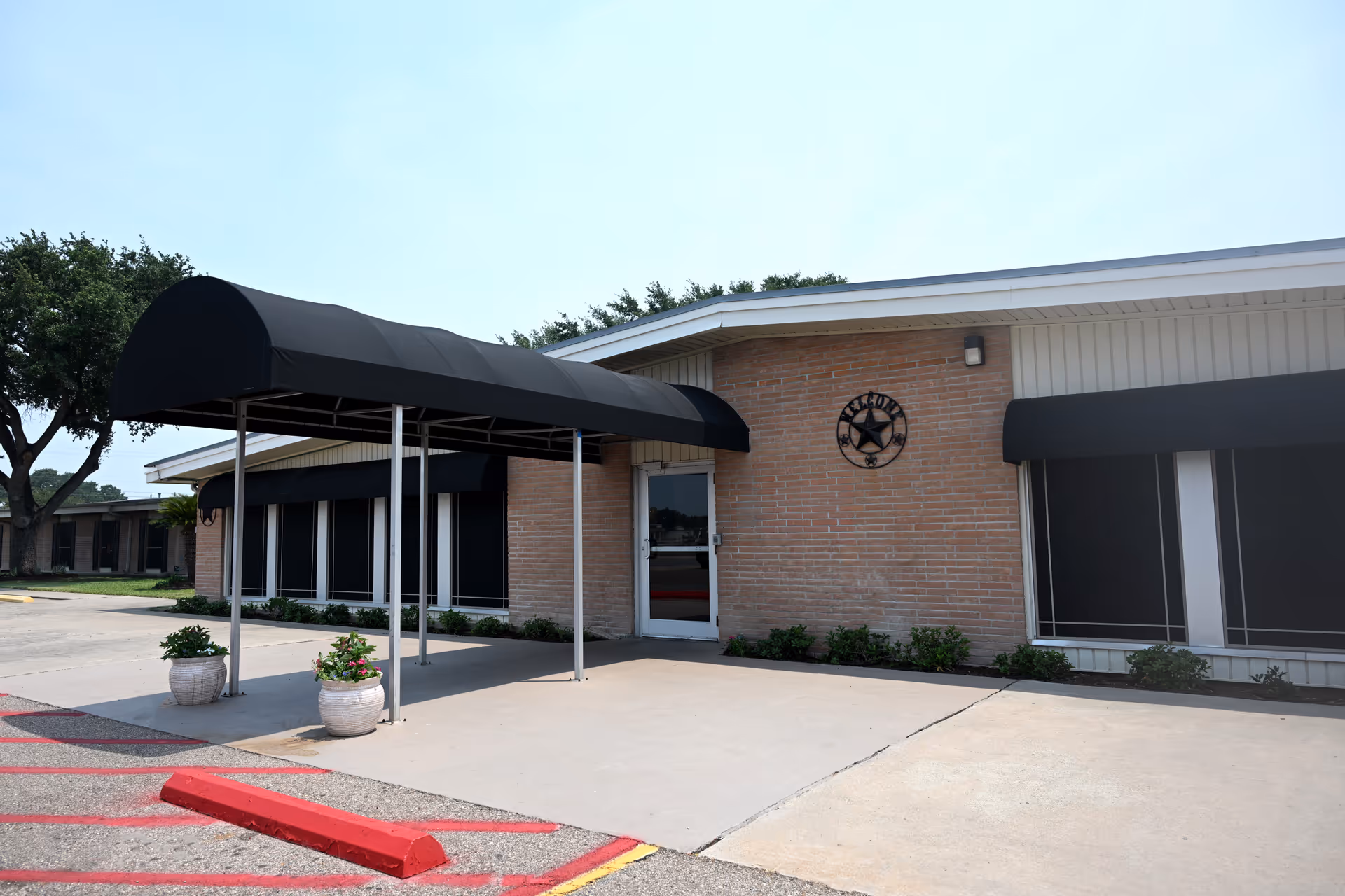 Front entrance of a single-story brick nursing facility with a black awning and a decorative star emblem above the door.