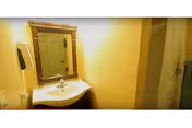 Small bathroom with a vanity sink, framed mirror, soap dispenser and a shower curtain in a yellow-painted room.